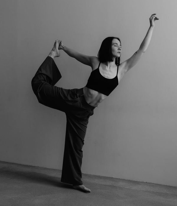 Woman in a graceful yoga tree pose against a minimal background.